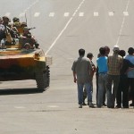 Kyrgyz soldiers on an armored vehicle drive past a group of people in Osh on June 11
